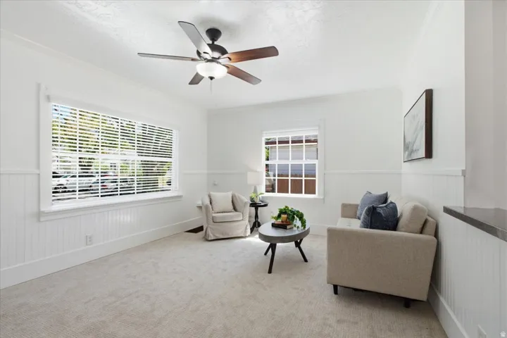 Inviting interior featuring recessed lighting, crown molding, white wainscoting, a wood-finish ceiling fan, and carpet flooring.
