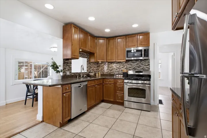 Kitchen featuring wood cabinetry, stainless steel appliances, mosaic tile backsplash, and a breakfast bar with a granite countertop.
