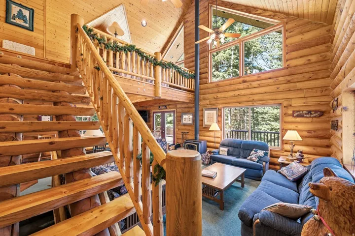 Interior featuring exposed log walls, a log staircase with railing, wood-finish vaulted ceilings, and large fixed-pane windows