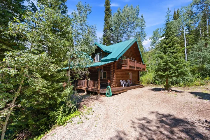 Log cabin exterior with a green metal roof, a ground-level wood deck, and a second-story balcony