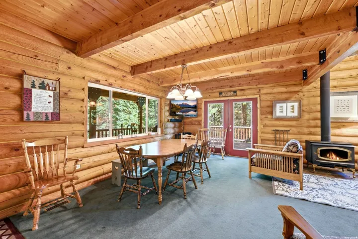 Interior features log walls, wood-paneled ceiling, exposed wood beams, and a wood-burning stove