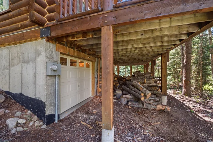 Log construction, concrete foundation, paneled garage door, wood deck structure, forested surroundings