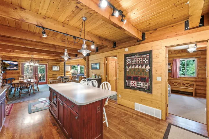 Spacious room featuring wood-finish flooring, exposed wood beam ceiling, wood plank walls, and a large kitchen island with seating