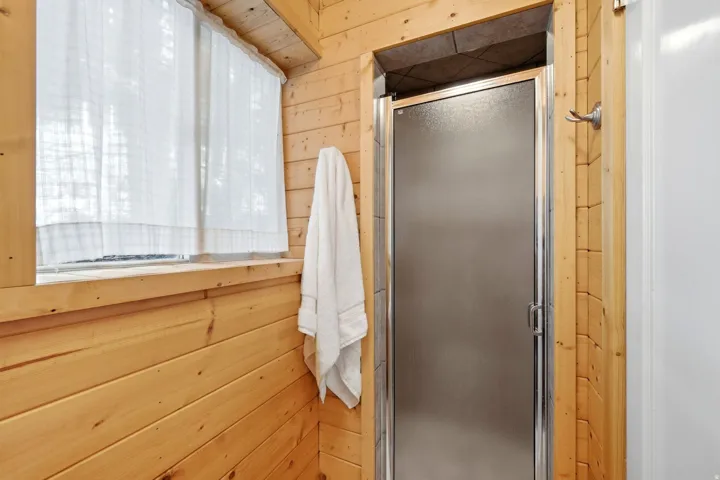 Wood-paneled wall accents a shower enclosure with a frosted glass door and chrome hardware