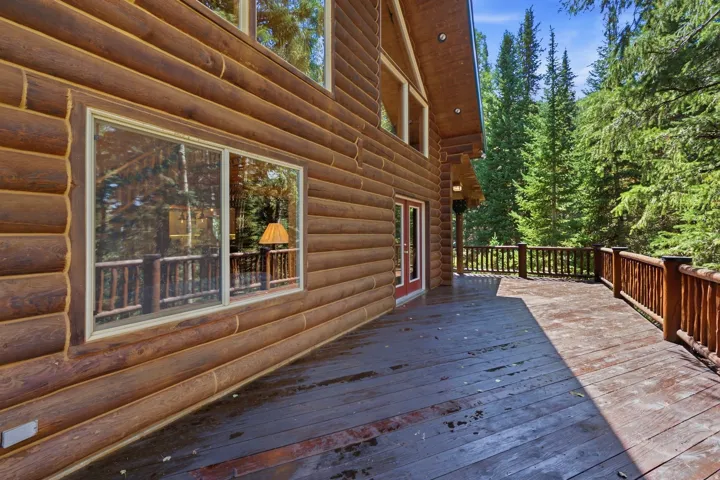Expansive outdoor deck with natural wood railing, set against a log-sided exterior with red double doors and multiple windows