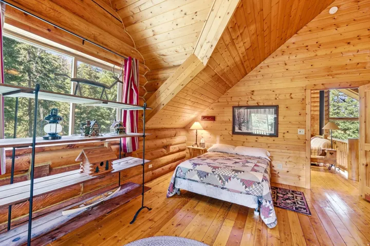 Wood-paneled walls and ceiling with exposed log construction, wood-finish flooring, and a window overlooking exterior scenery