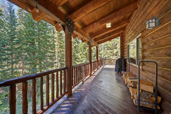 Expansive wood deck with a natural wood railing, log-style exterior siding, and exposed wood beam ceiling