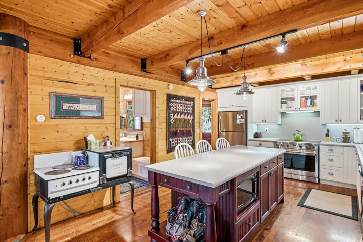 Open-concept kitchen with wood plank walls, exposed wood beams, wood-finish flooring, a central island with countertop, and white shaker-style cabinetry