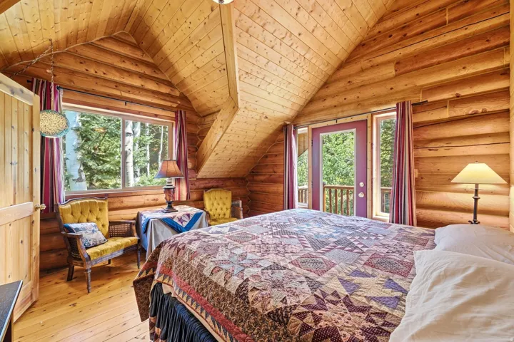 Vaulted wood-paneled ceiling, log-style wall construction, wood-finish flooring, large window with outdoor scenery, and a glass-paneled exterior door