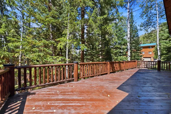 Expansive wood-finish deck with natural wood railings, surrounded by mature trees