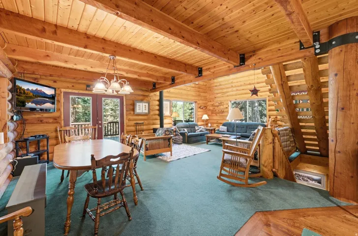 Expansive interior featuring exposed log walls, wood-finish flooring, a prominent wood staircase, and a vaulted wood-paneled ceiling
