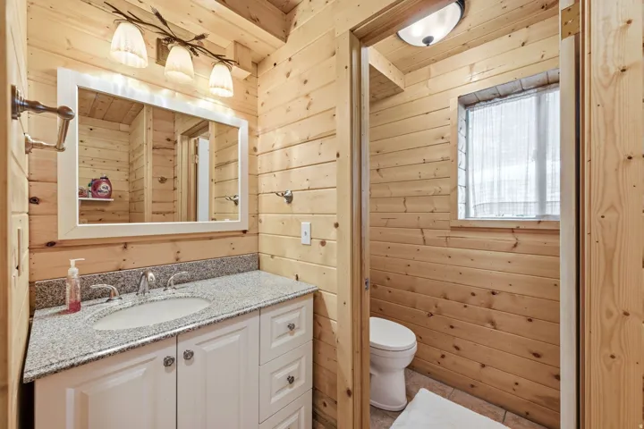 Wood-paneled bathroom featuring a white vanity with a light-toned countertop, an oval undermount sink, and a framed mirror