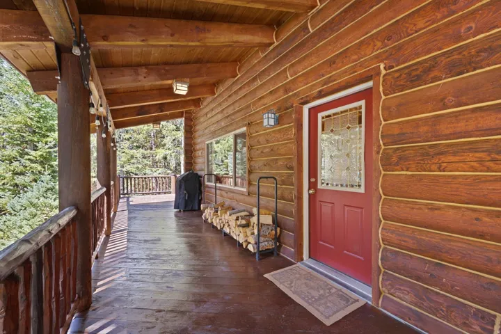 Expansive wood-plank deck featuring log railings, a red entry door with decorative glass, and a log-sided exterior