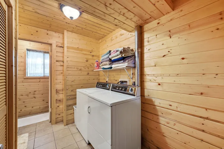Laundry room featuring wood paneling, tiled flooring, built-in shelving, and a louvered door