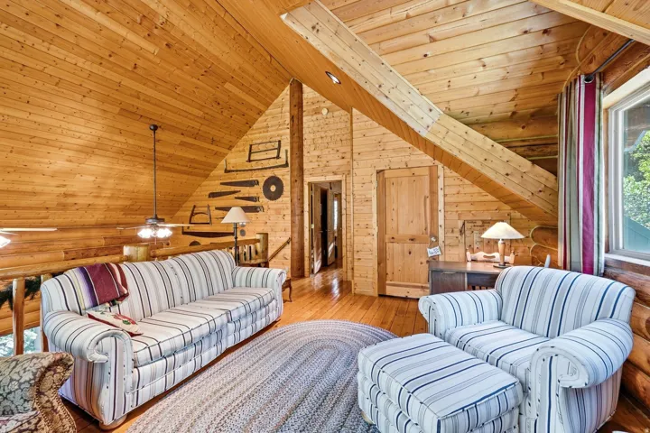 Wood-paneled walls and ceiling, exposed structural beams, hardwood flooring, and a multi-pane window