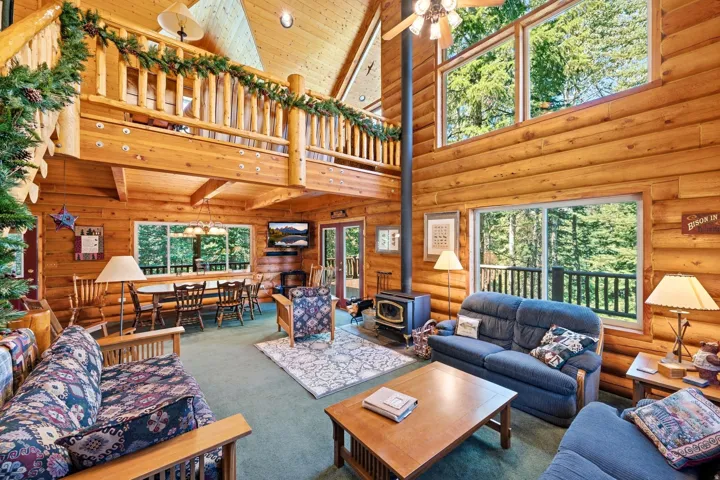 Open-concept living space featuring wood-paneled walls and ceiling, a wood-burning stove, and expansive windows
