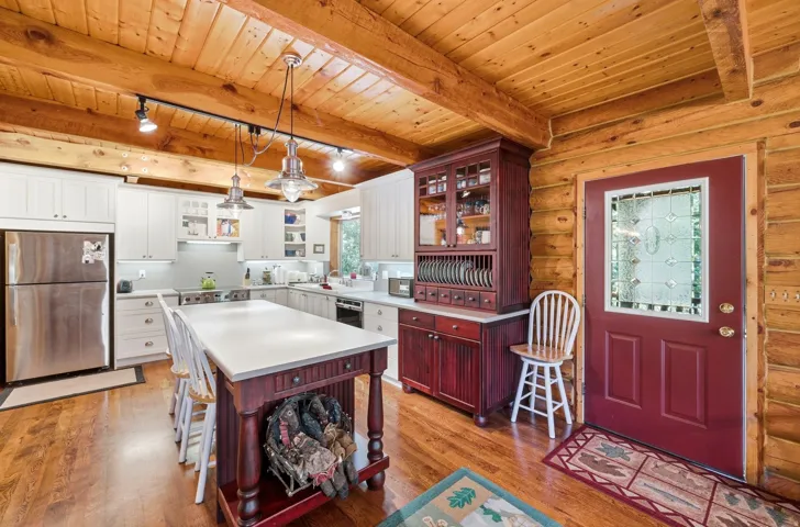 Wood-plank ceiling with exposed beams, wood-finish flooring, white cabinetry, stainless steel appliances, and a leaded glass entry door