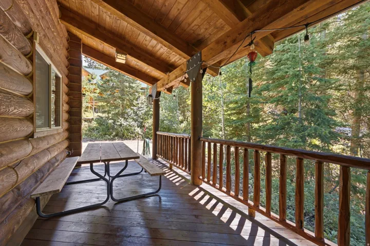 Wood-finish siding with a covered porch featuring exposed wood beams, wood-finish flooring, and a wood-finish railing