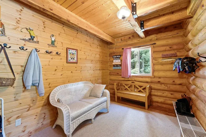 Wood-paneled walls and ceiling with exposed beam, a single window, and neutral-toned carpeting