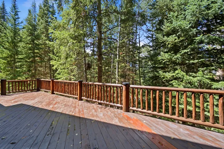 Expansive outdoor deck featuring wood-finish flooring and rustic log railings, surrounded by mature trees
