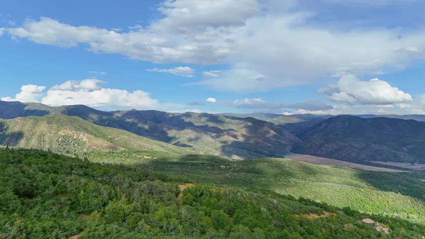 Expansive mountain landscape with diverse foliage, distant valleys, and a partially visible structure within the natural terrain