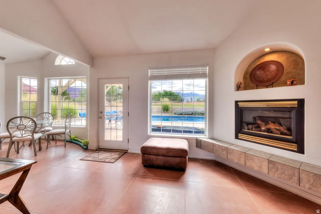 Vaulted ceiling with an arched transom window, built-in fireplace with a tiled hearth, and multiple windows offering expansive outdoor views including a pool