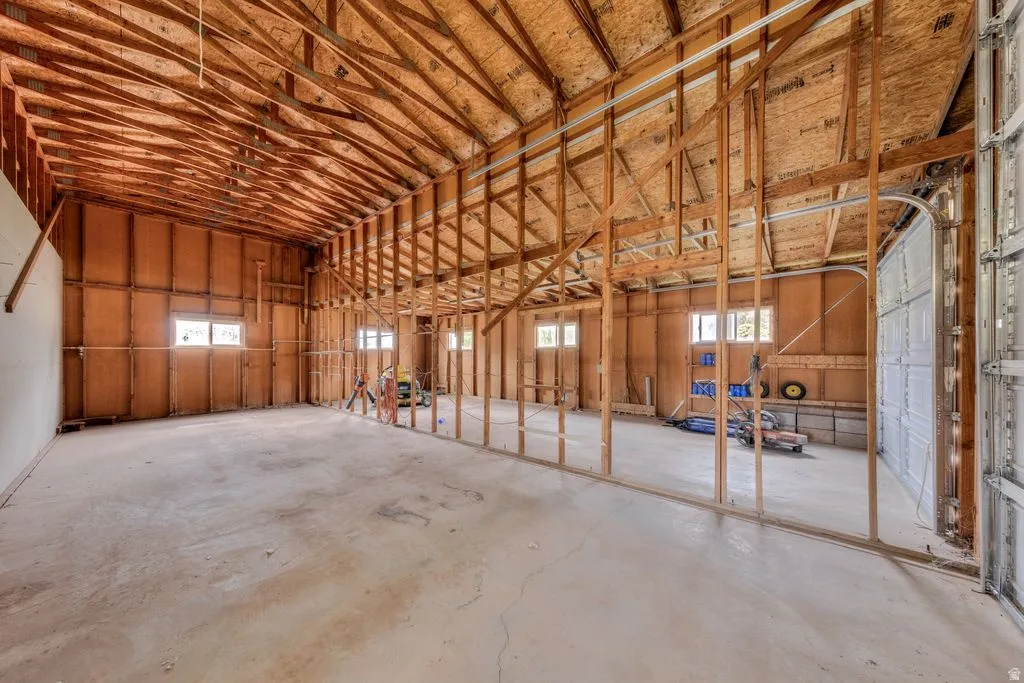Spacious interior framing with exposed ceiling trusses, concrete flooring, multiple windows, and a large garage door opening