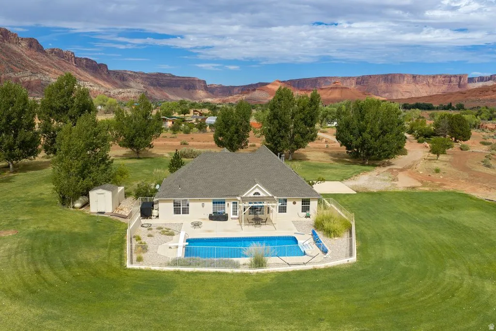Expansive green lawn surrounding a residence with a large outdoor pool, fenced enclosure, and a patio space
