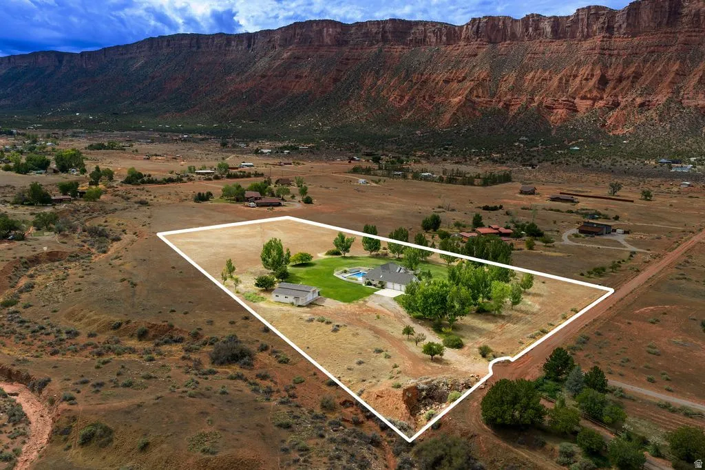 Expansive property featuring a single-story residence, a detached auxiliary building, an in-ground swimming pool, and mature trees, set against a backdrop of natural rock formations
