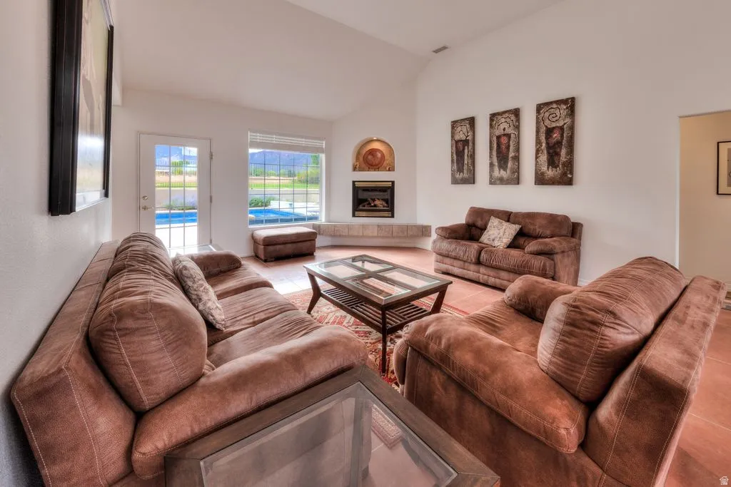 Vaulted ceiling with a fireplace, built-in shelving, glass-paned door, and tiled flooring