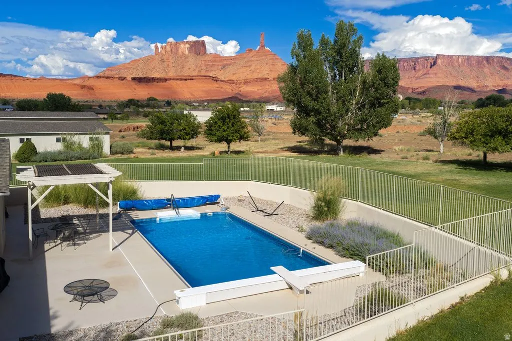 In-ground swimming pool with diving board, surrounded by concrete decking and metal fencing