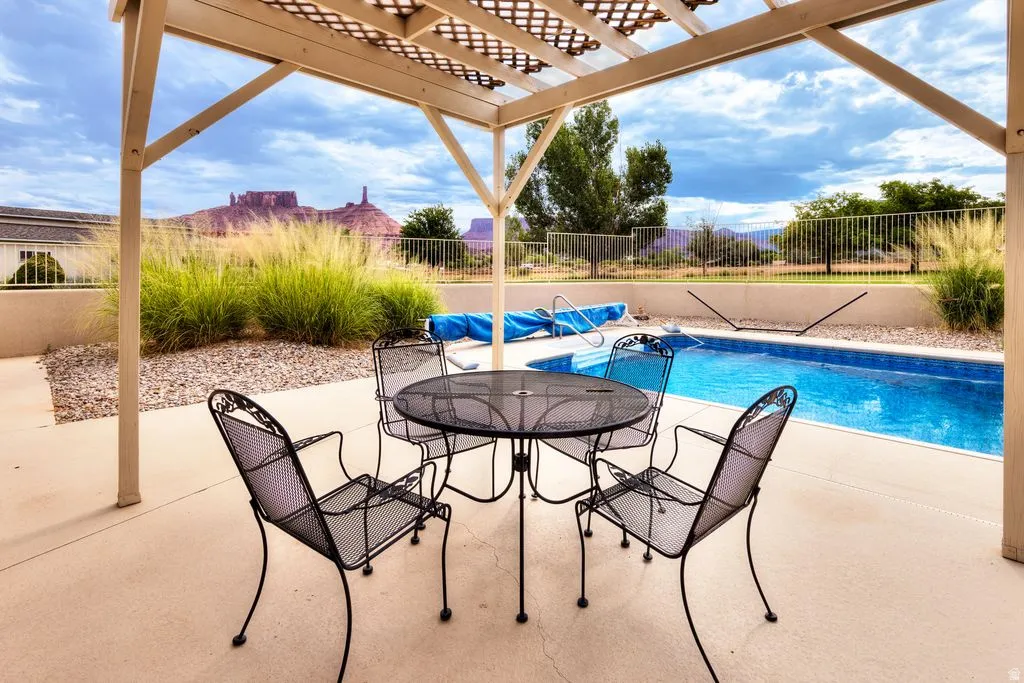 Covered patio with an outdoor swimming pool, concrete hardscaping, and a distant mountain backdrop