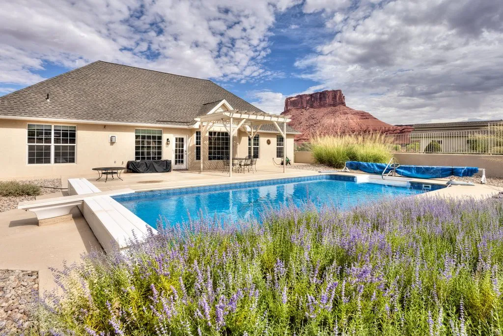 Outdoor swimming pool with a diving board, surrounding concrete patio, and a white pergola