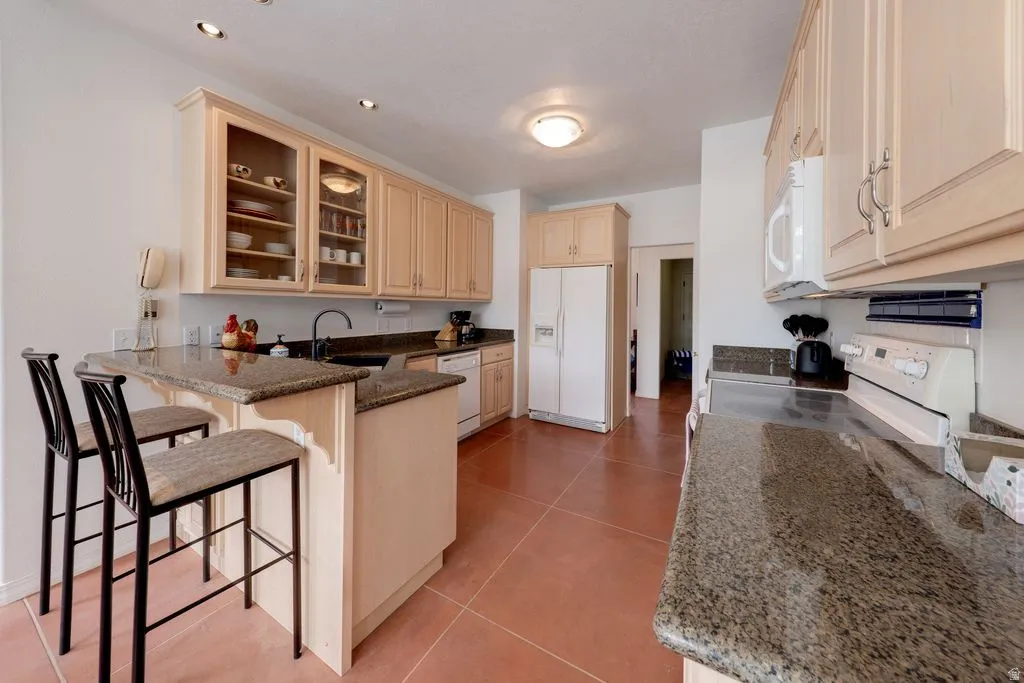 Kitchen featuring wood-finish cabinetry, granite countertops, recessed lighting, and a breakfast bar
