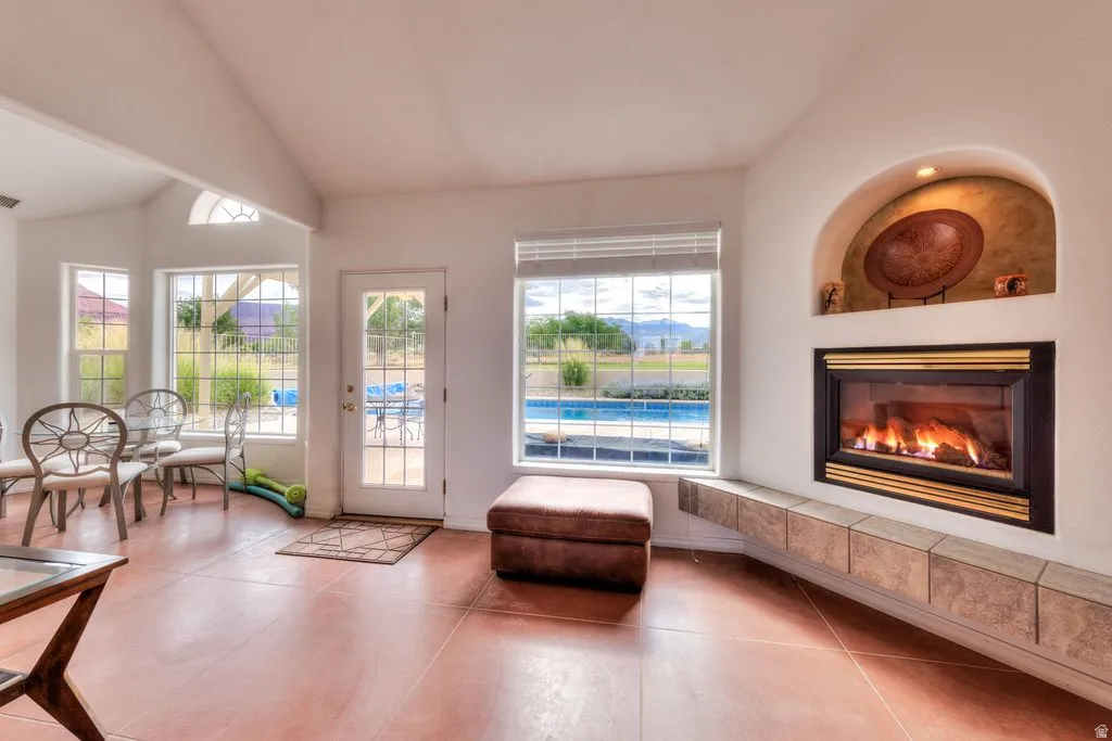 Vaulted ceiling, multiple large windows, a built-in fireplace with a stone-finish hearth, and exterior access to a swimming pool
