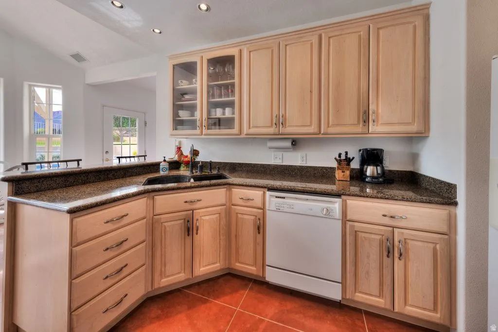 Kitchen featuring wood cabinetry, granite-style countertops, integrated dishwasher, and tile flooring