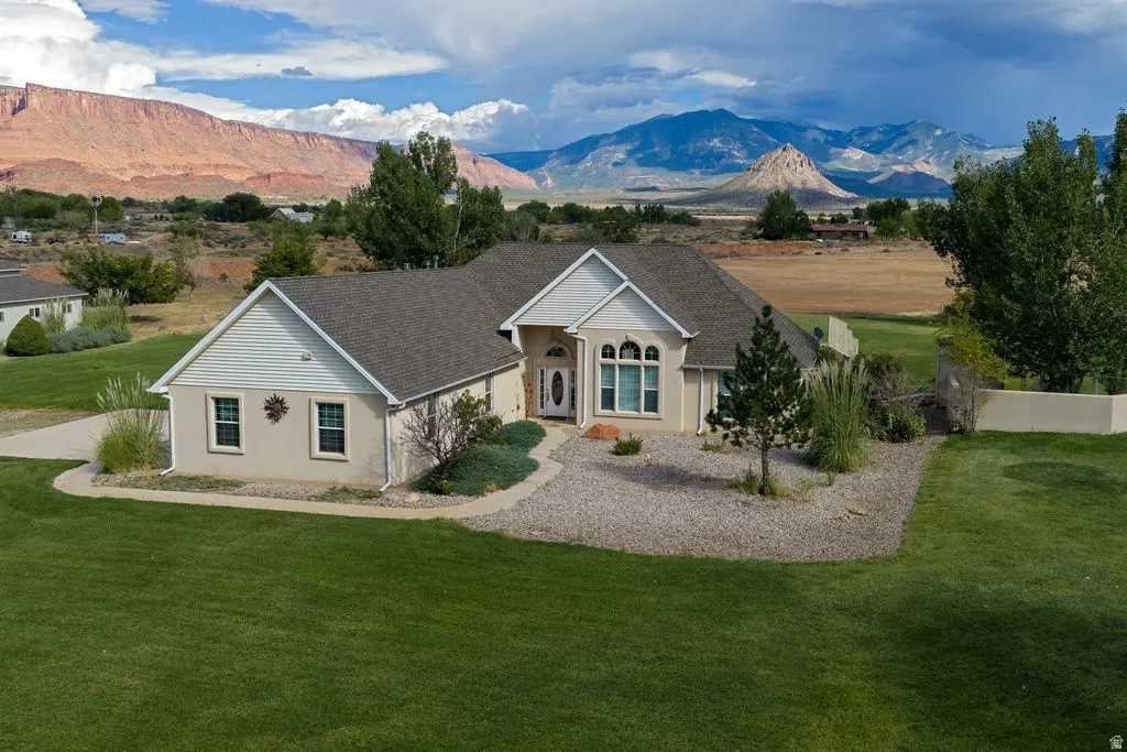 Stucco and siding exterior with a dark shingle roof, arched transom window, and mature landscaping