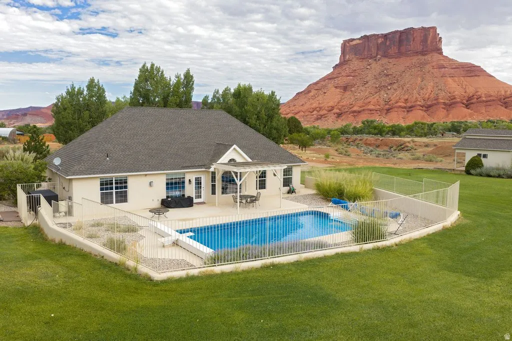 Expansive backyard with a fenced in-ground swimming pool, concrete patio, and pergola