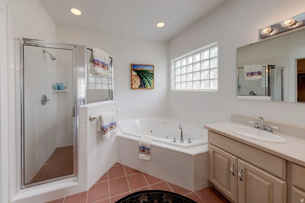 Walk-in shower with glass enclosure, soaking tub, glass block window, single vanity with integrated sink, and terra cotta tile flooring