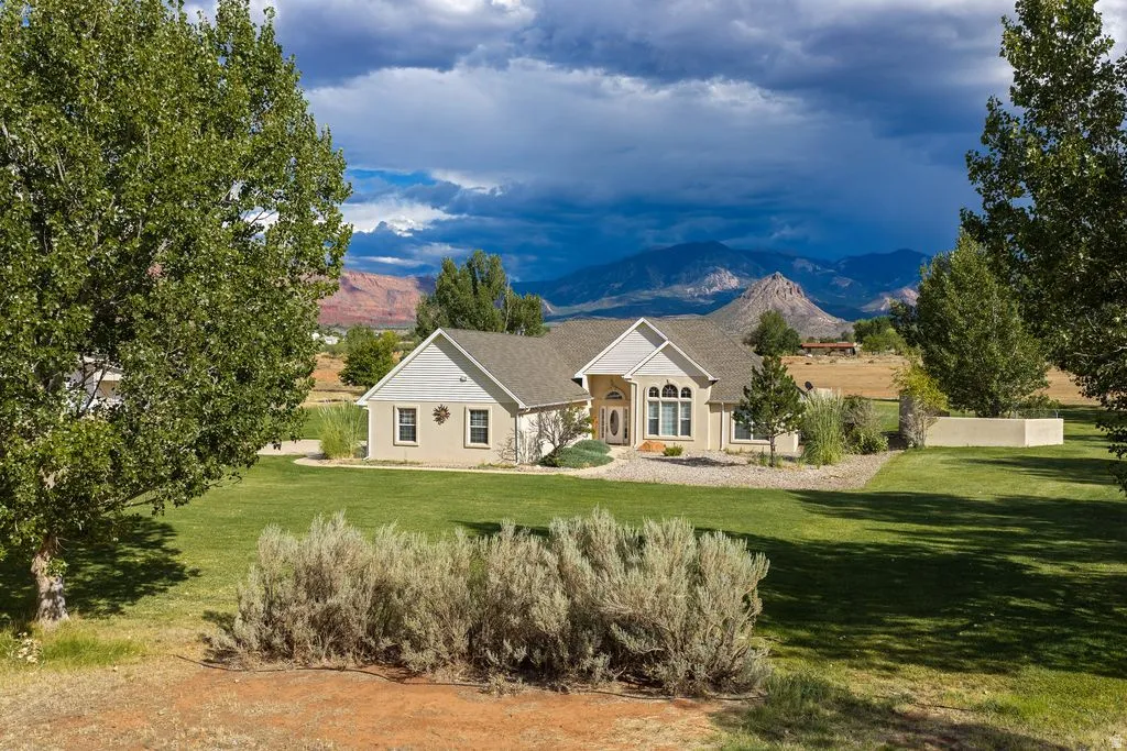Expansive green lawn with mature trees and shrubbery, featuring a stucco exterior and mountain scenery