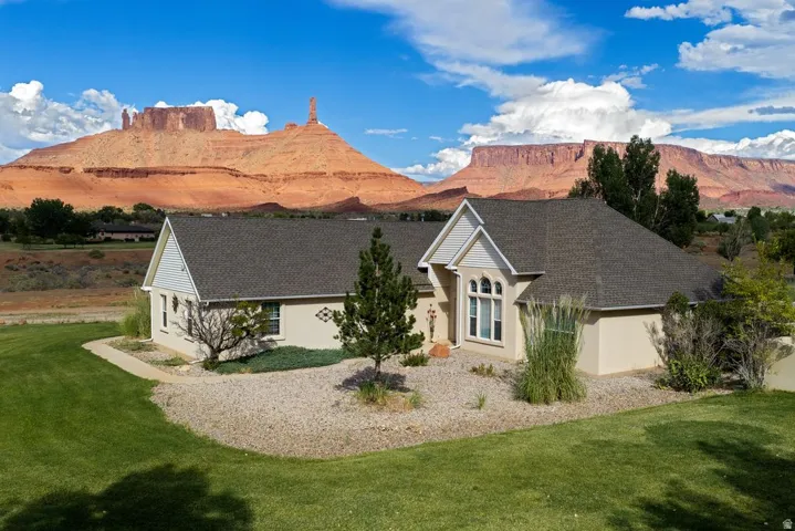 Stucco exterior with a pitched shingle roof, arched multi-pane window, and a gravel and grass landscape