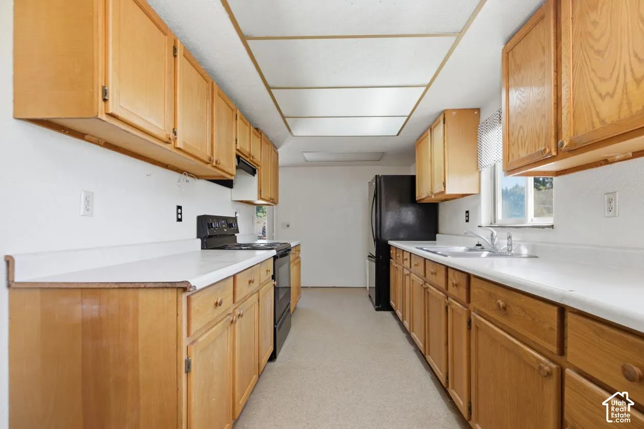 Galley kitchen featuring wood cabinetry, white countertops, a double basin sink, and a black range