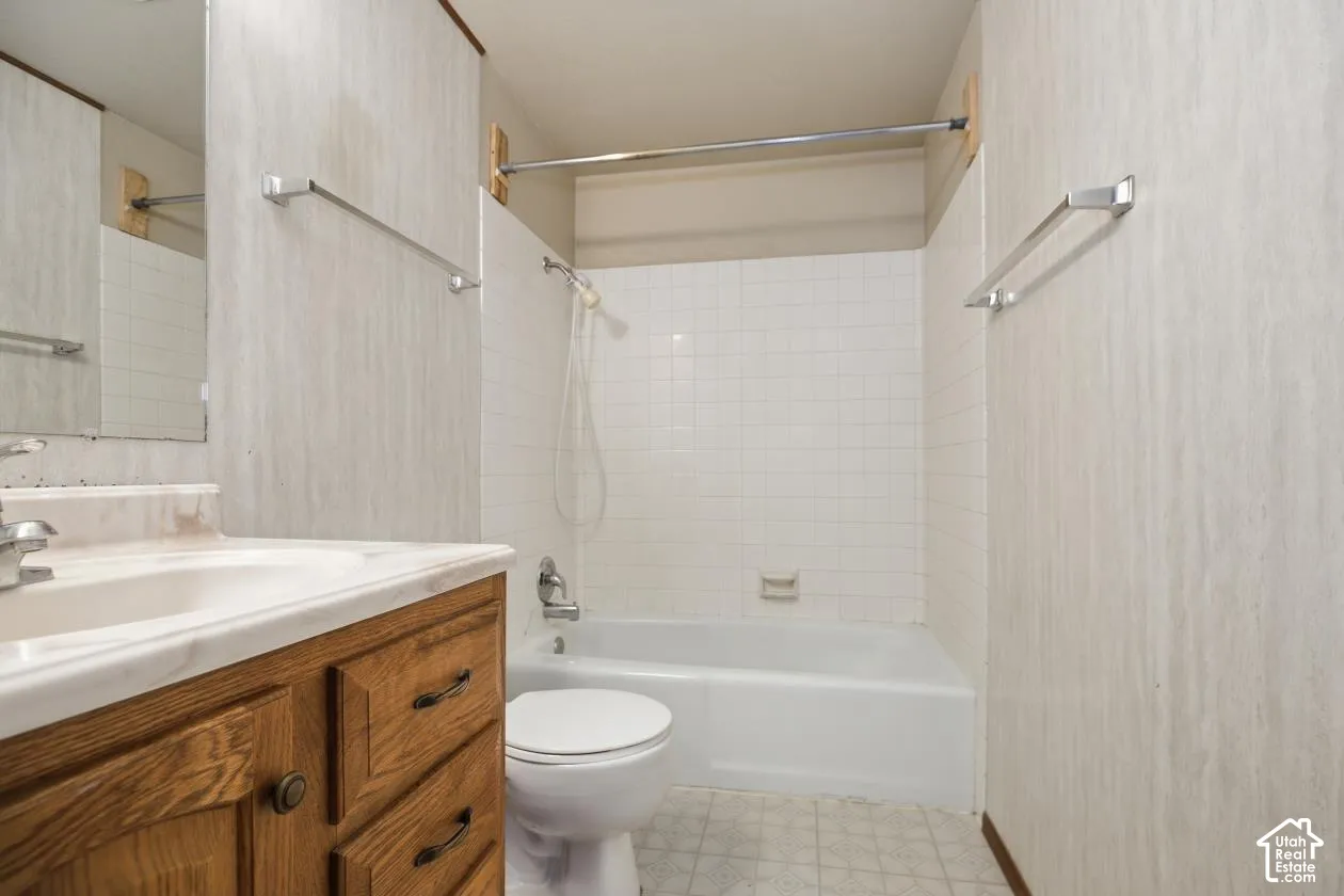 Bright and updated bathroom featuring a wood-finish vanity with dual-sink countertop, white subway tile surround, and a combined tub-shower enclosure with chrome fixtures and glass surround panel