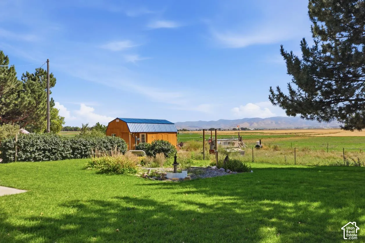 Expansive green lawn with mature landscaping, a wood-sided outbuilding with a blue metal roof, and distant mountain ranges