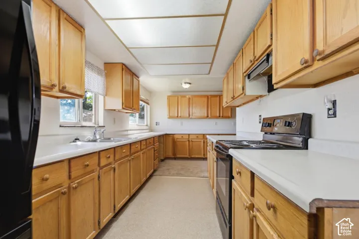 Galley kitchen with wood-finish cabinetry, white countertops, built-in double basin sink, and a four-burner electric range