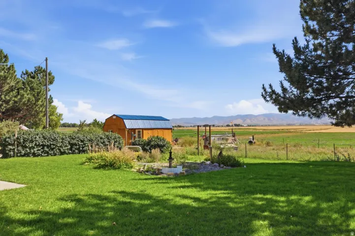 Expansive green lawn with mature landscaping, a wood-sided outbuilding with a blue metal roof, and distant mountain ranges
