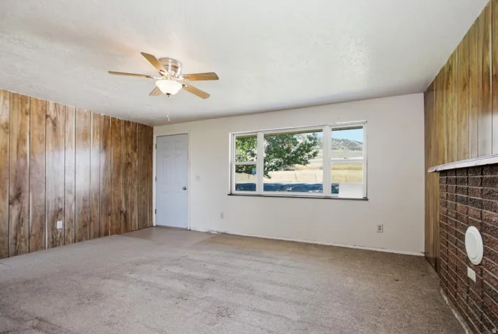 Interior space featuring wood-panel accent walls, a ceiling fan with integrated lighting, and a large window