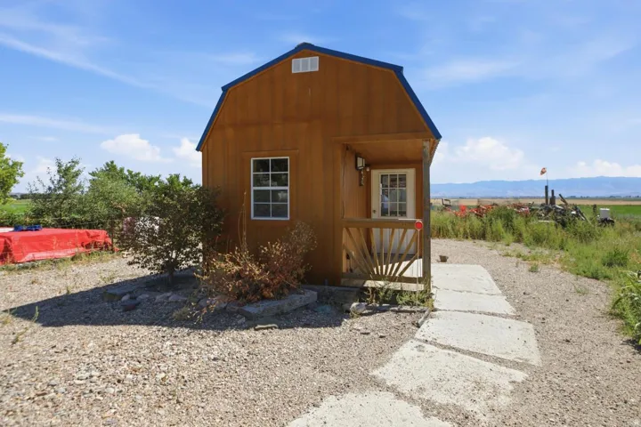 Wood-sided building with a blue gambrel roof, featuring a small covered porch and a white entry door