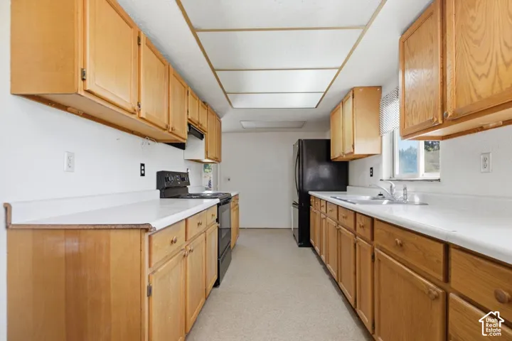 Galley kitchen featuring wood cabinetry, white countertops, a double basin sink, and a black range