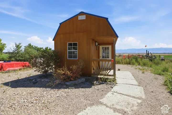 Wood-sided building with a blue gambrel roof, featuring a small covered porch and a white entry door